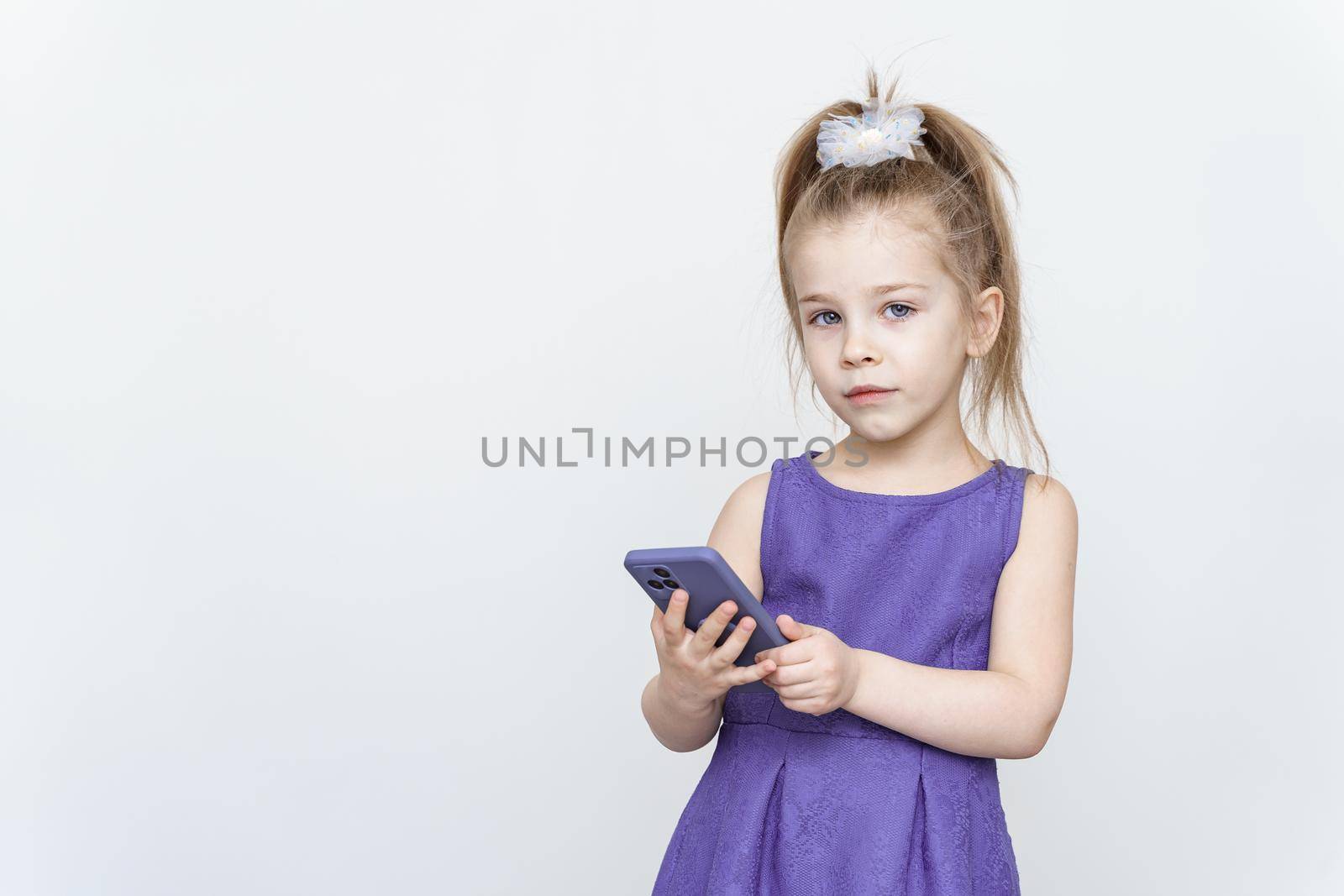 cute 5-6 year old girl in a blue dress posing in the studio with a smartphone by Lena_Ogurtsova