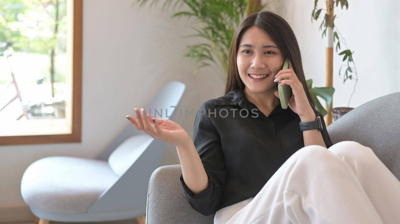 Cheerful young woman having cell phone conversation while sitting on couch at home.
