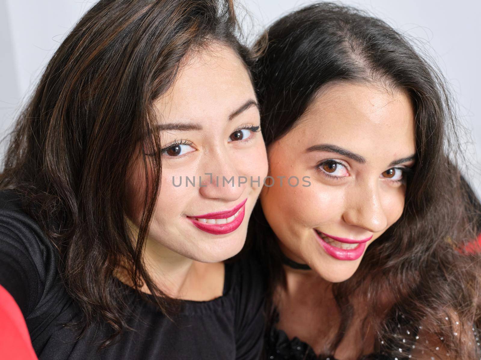 Front view of two latin female friends taking a selfie and looking at camera in black dresses on Halloween