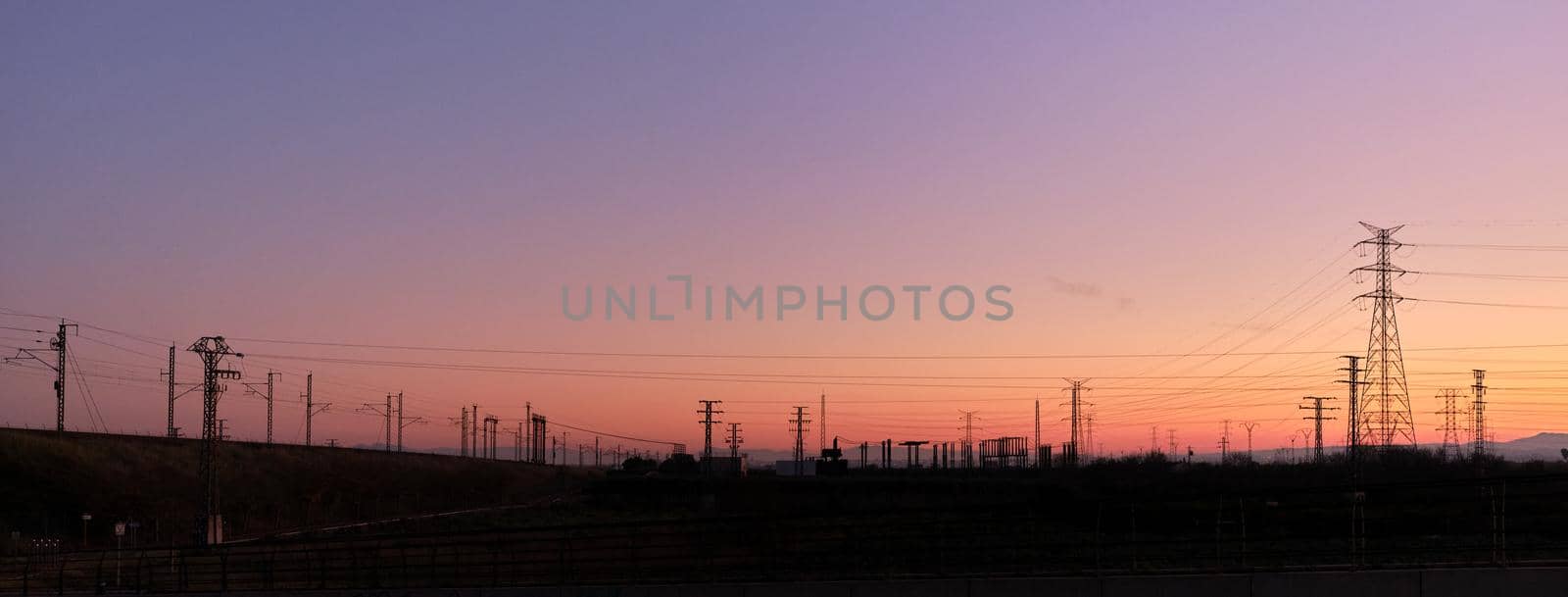 Panoramic photo of a vivid sunset with silhouettes of electric towers on the background