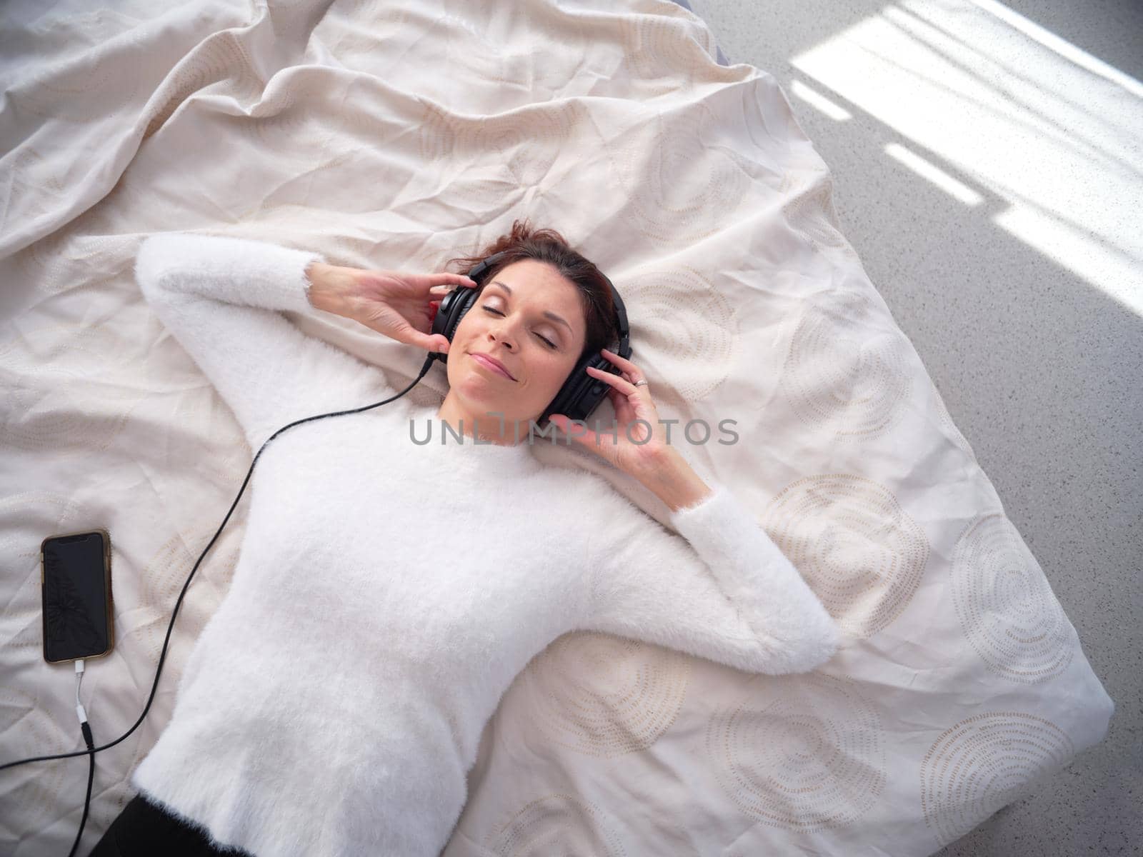 Woman relaxed on the bed with eyes closed and listening to music with the mobile by WesternExoticStockers