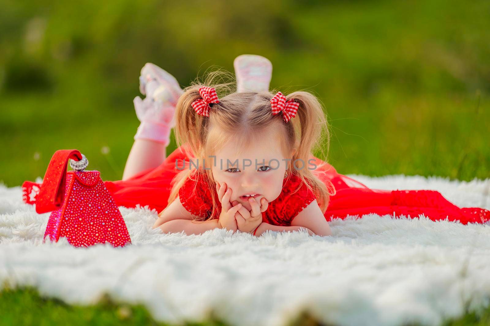 a girl in a red dress lies on a white blanket that is laid on the lawn