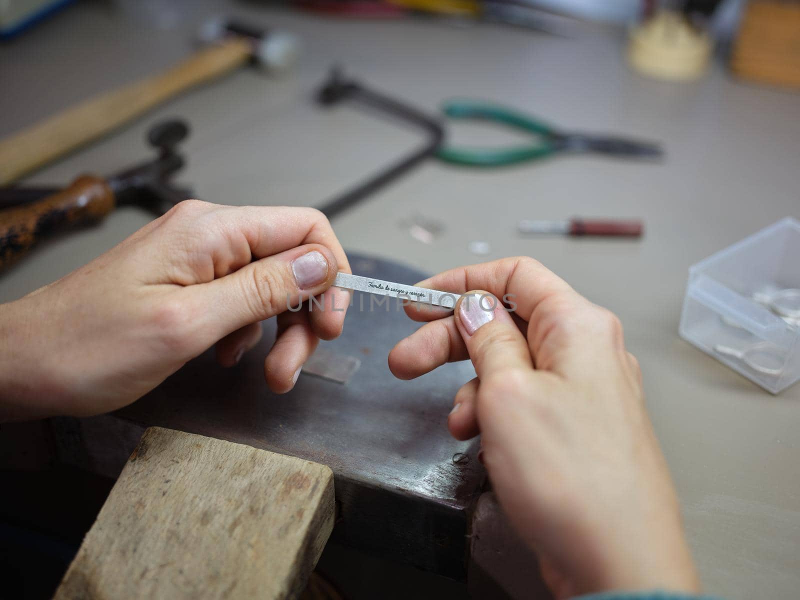 Unrecognizable adult worker woman working in her jewelry artisan workshop holding a piece of metal with the inscription "Familia de sangre y corazon" in spanish wich tanslation is "Family of blood and heart"