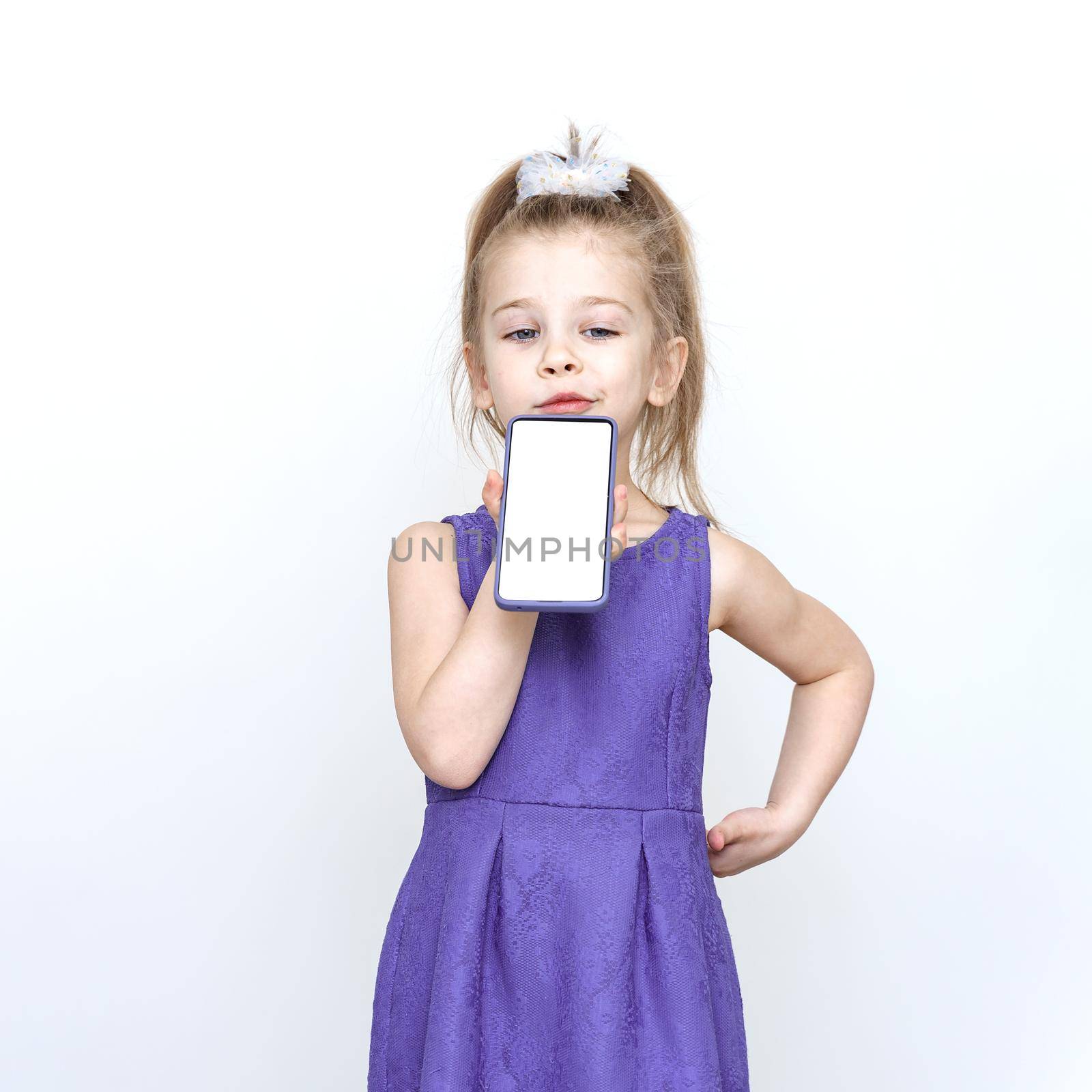 cute 5-6 year old girl in a blue dress posing in the studio. child talking on speakerphone, smartphone mockup