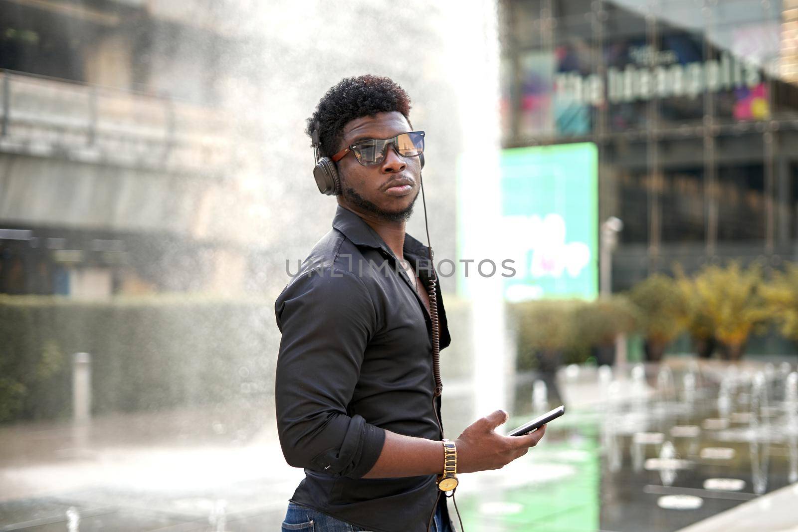 Serious african man holding a mobile while listening to music outside a shopping mall in Bangkok