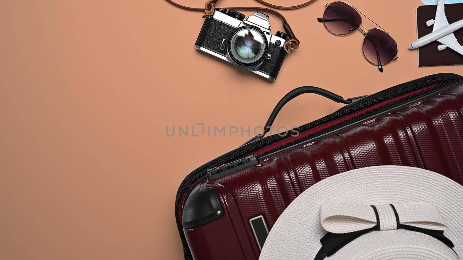 Above view suitcase with sunglasses, camera, passport and hat on beige background. Preparing for the summer vacations.