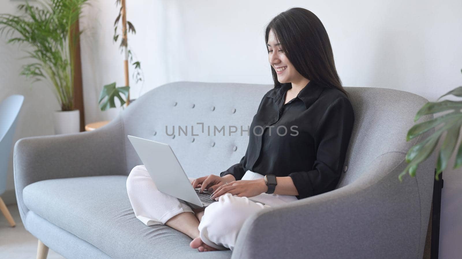 Happy young asian woman relaxing on couch and surfing internet, working online with computer laptop.