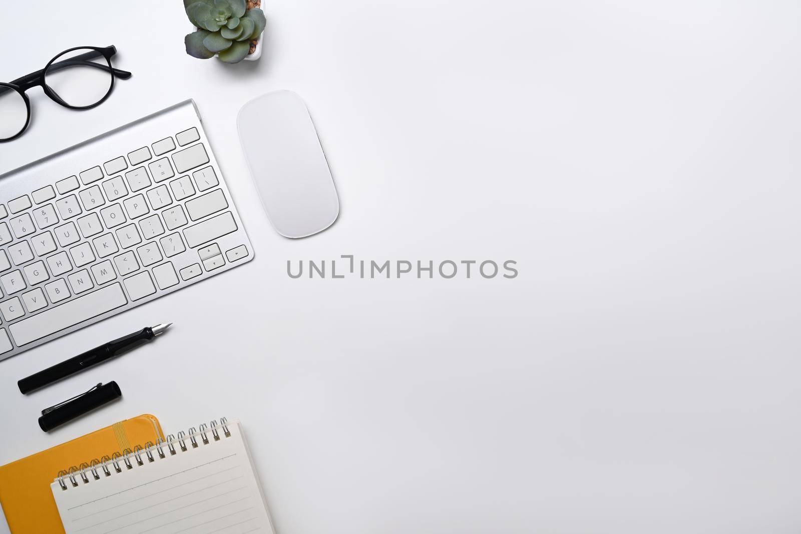 Top view white office desk with wireless keyboard, glasses, notebook and succulent plant.