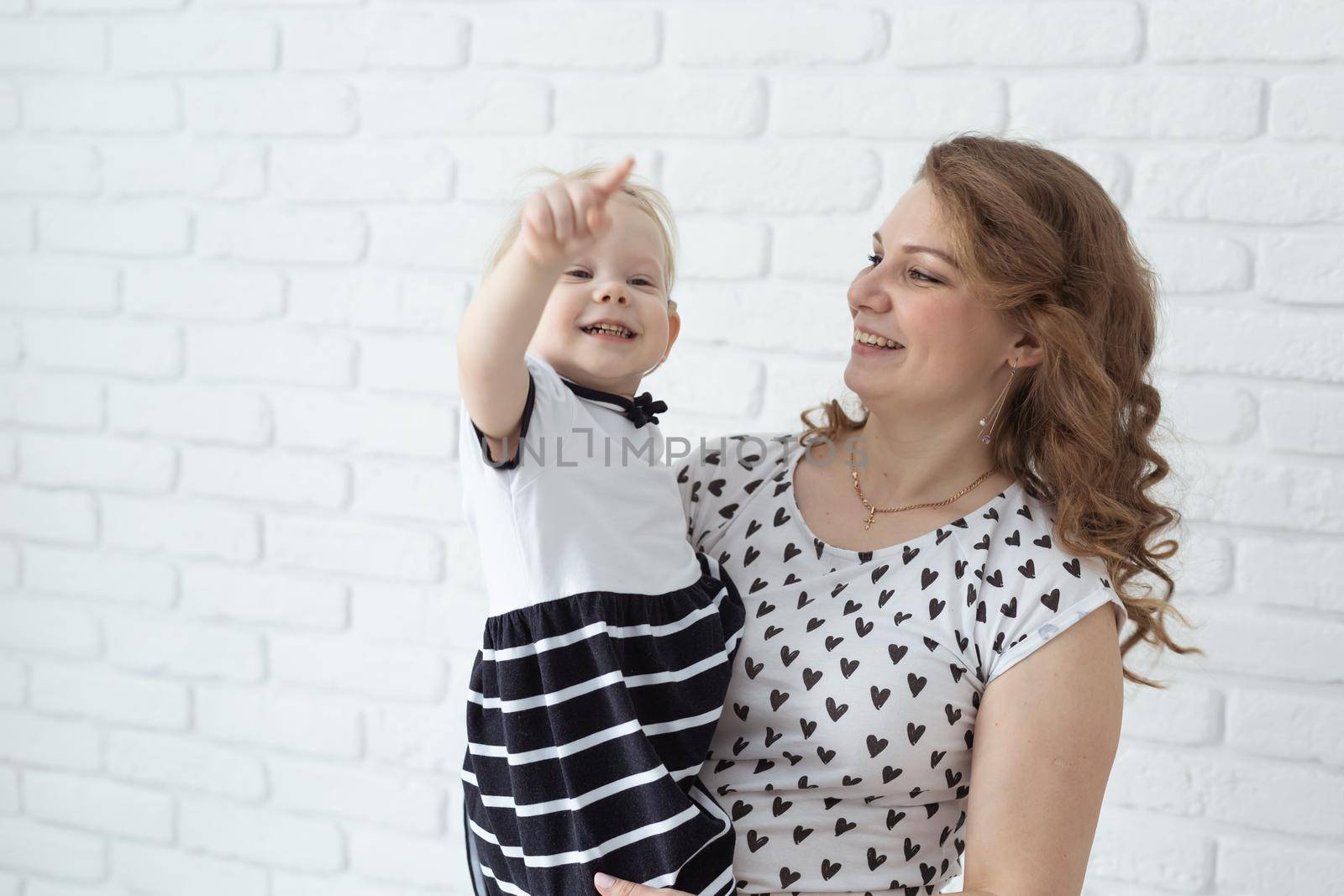 Mother holds and having fun her child with hearing aids and cochlear implants on white brick wall with copy space and place for advertising . Deaf and innovating medicine technologies concept by Satura86