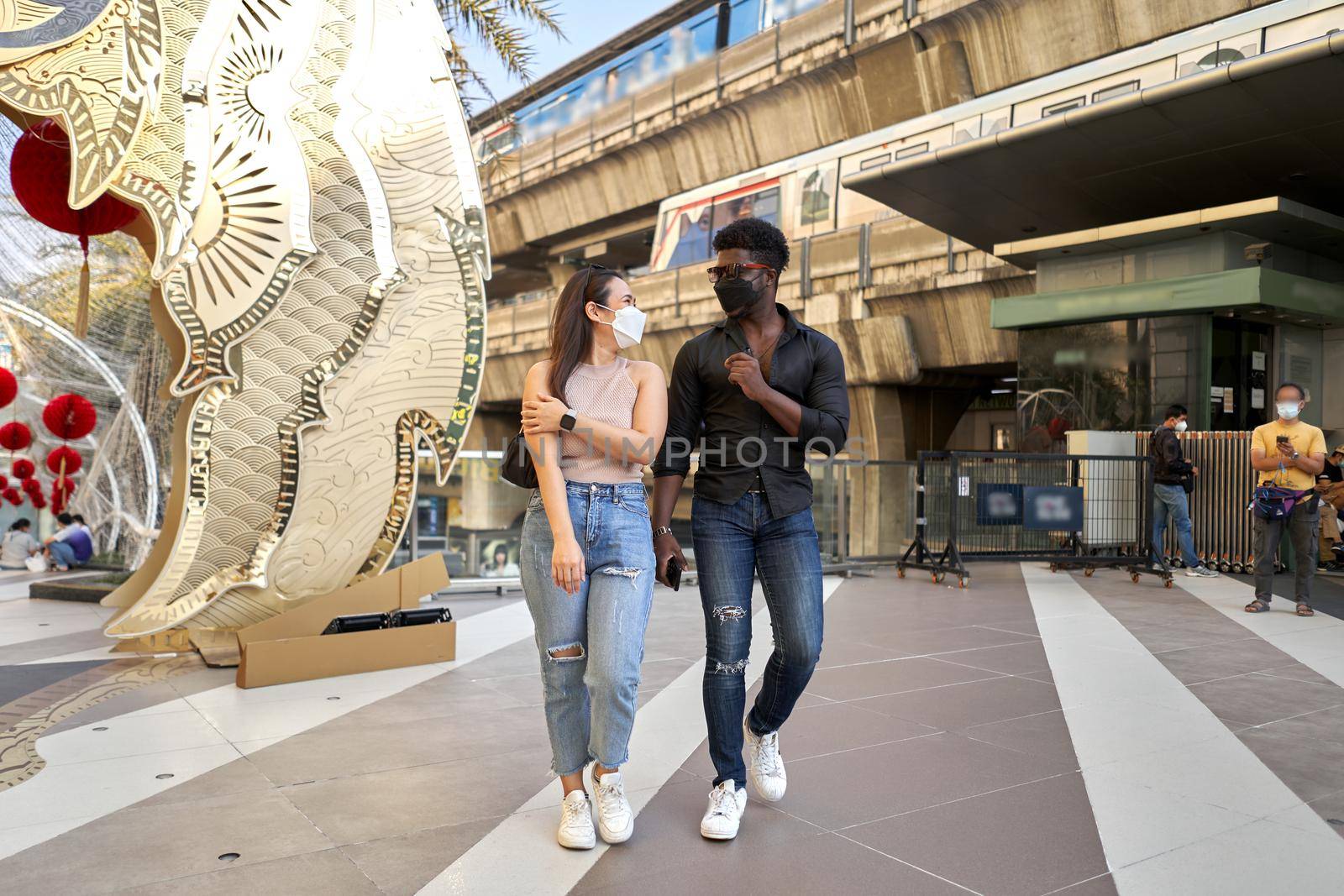 Two multiracial friends walking through an outdoor shopping mall using mask in Bangkok