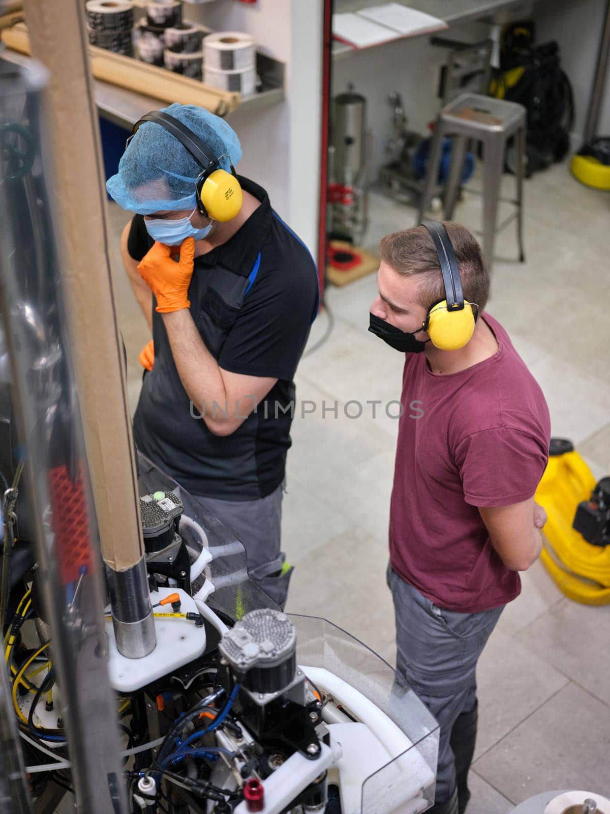 Vertical photo of two workers standing controlling the machinery of a craft beer packaging factory.