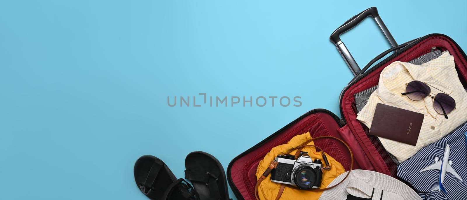 Open suitcase with camera, sunglasses, passport and clothes on blue background. Preparing for the summer vacations.