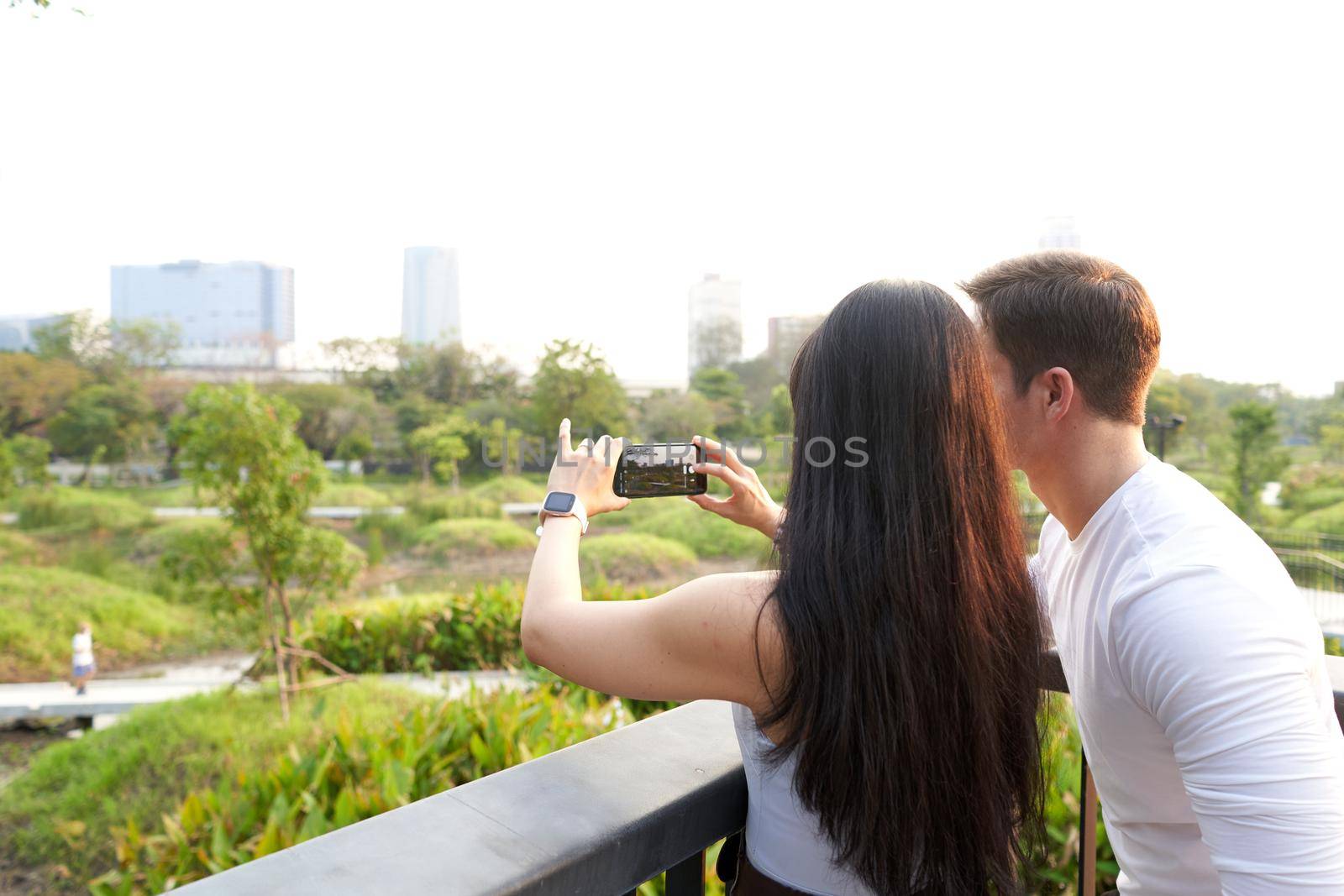 Multiethnic couple taking photos of the cityscape with skyscrapers from a park at sunset