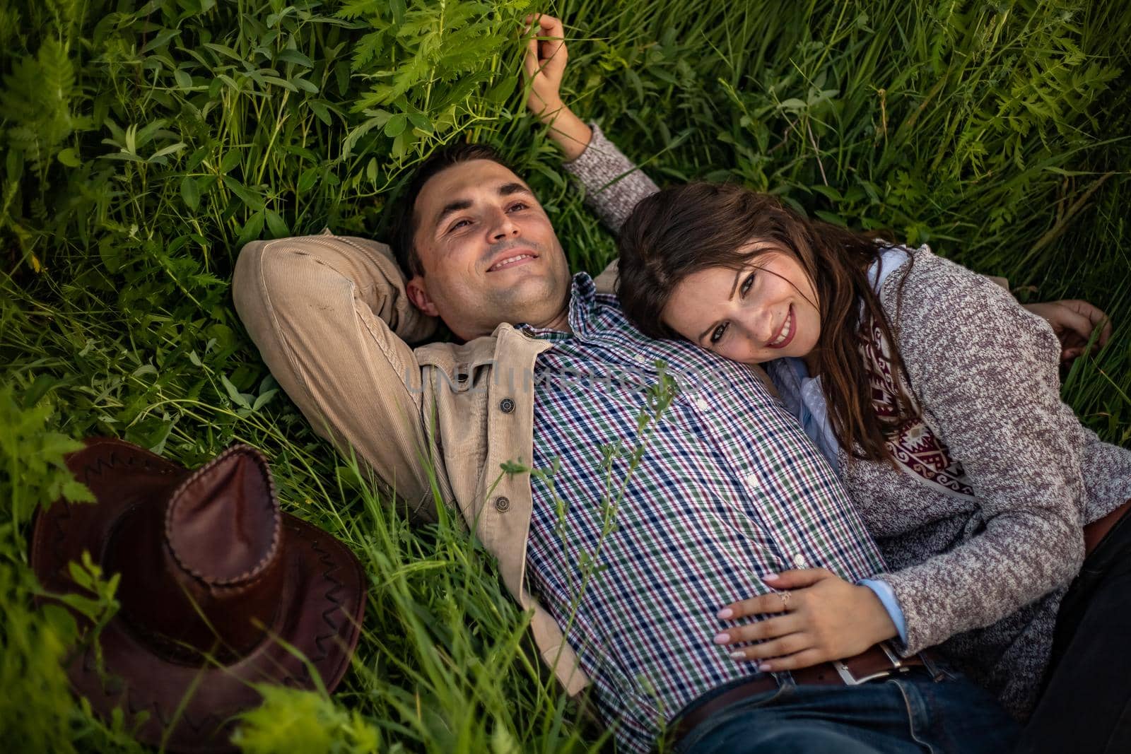 Young couple having picnic in meadow on bright sunny day. Man and woman enjoy each other's company