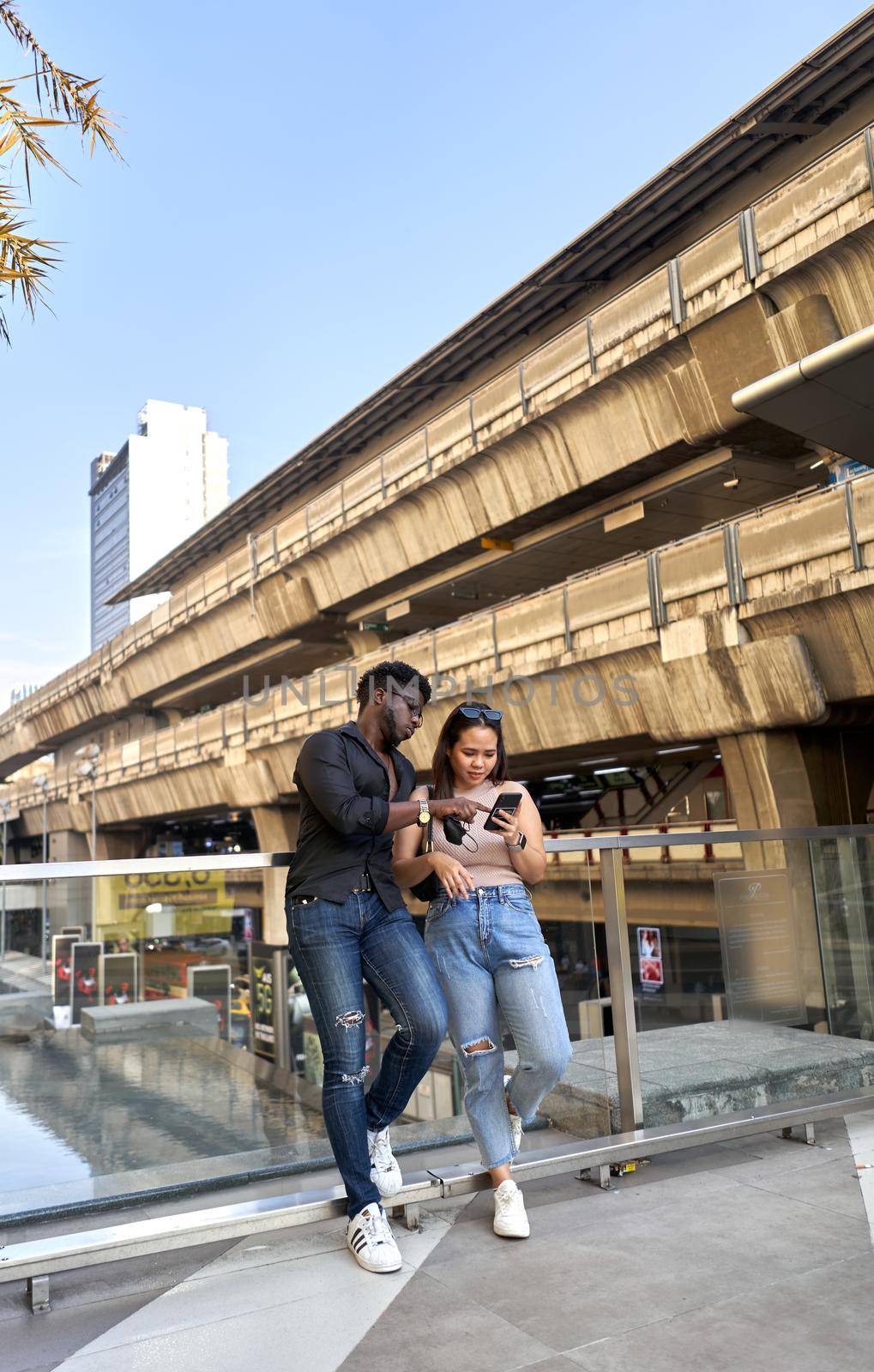 Vertical photo of two friends using a mobile in the entrance of a shopping mall in Bangkok, Thailand