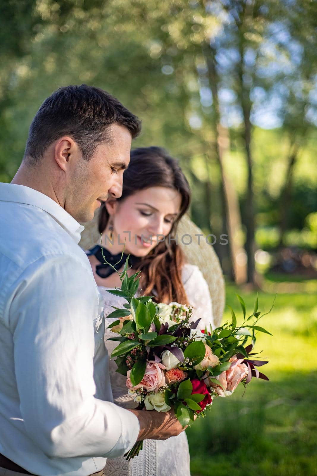 Happy young people in wedding dresses stand in the meadow and look at each other. portrait of a bride looking at a beautiful wedding bouquet by Anyatachka