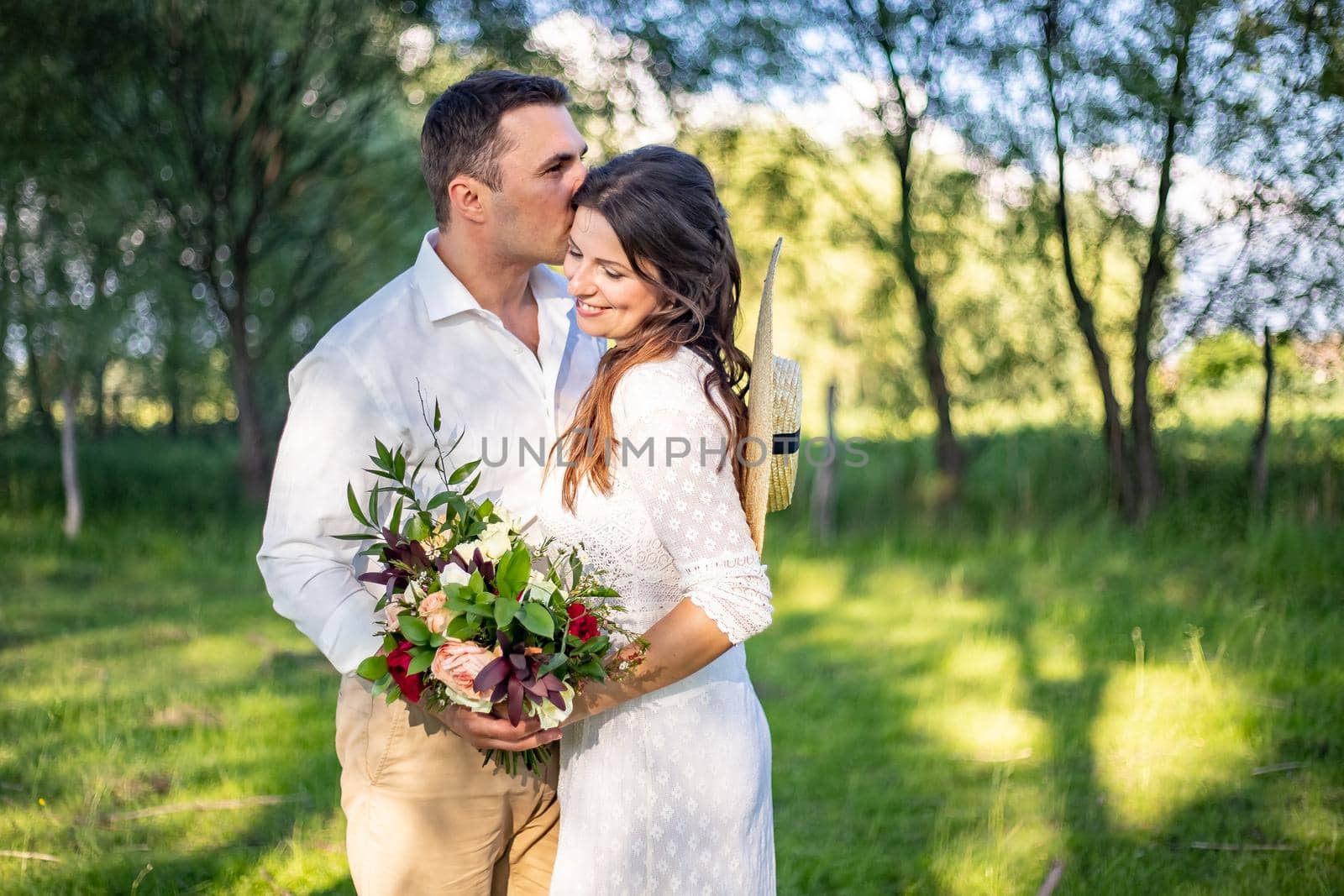 beautiful newlyweds stand on a green meadow and kiss, rustic style wedding by Anyatachka