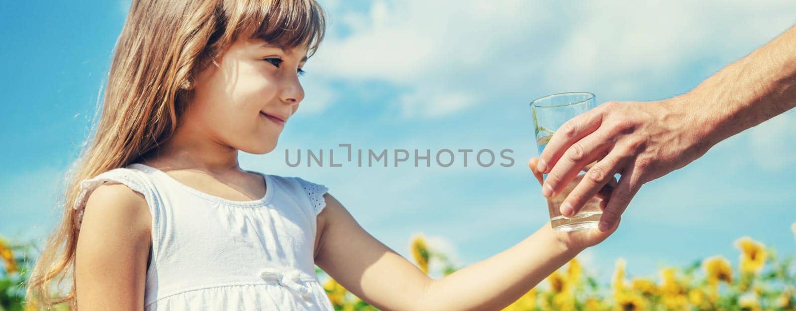 The father gives the child water in the background of the field. Selective focus.