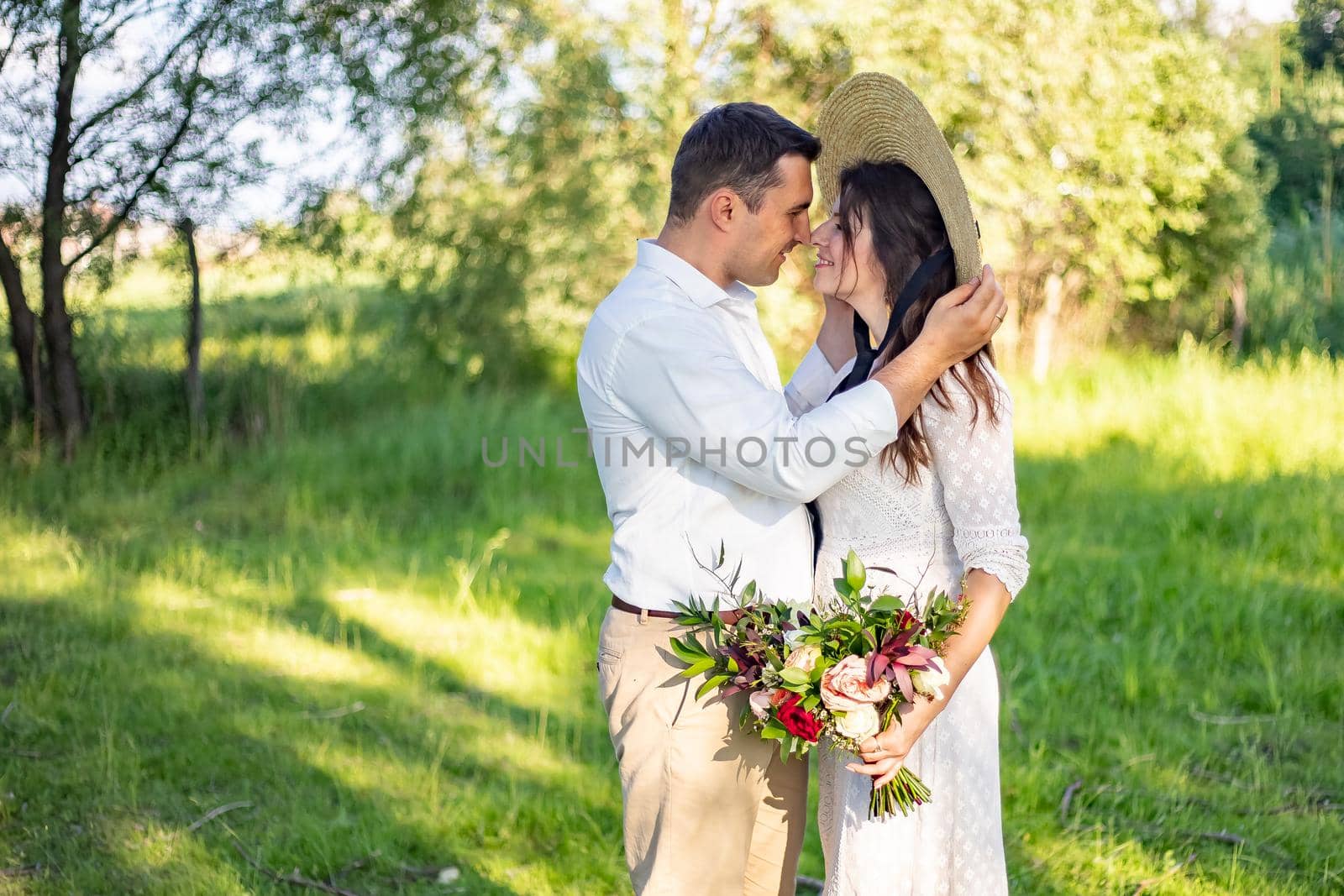 beautiful newlyweds stand on a green meadow and kiss, rustic style wedding by Anyatachka