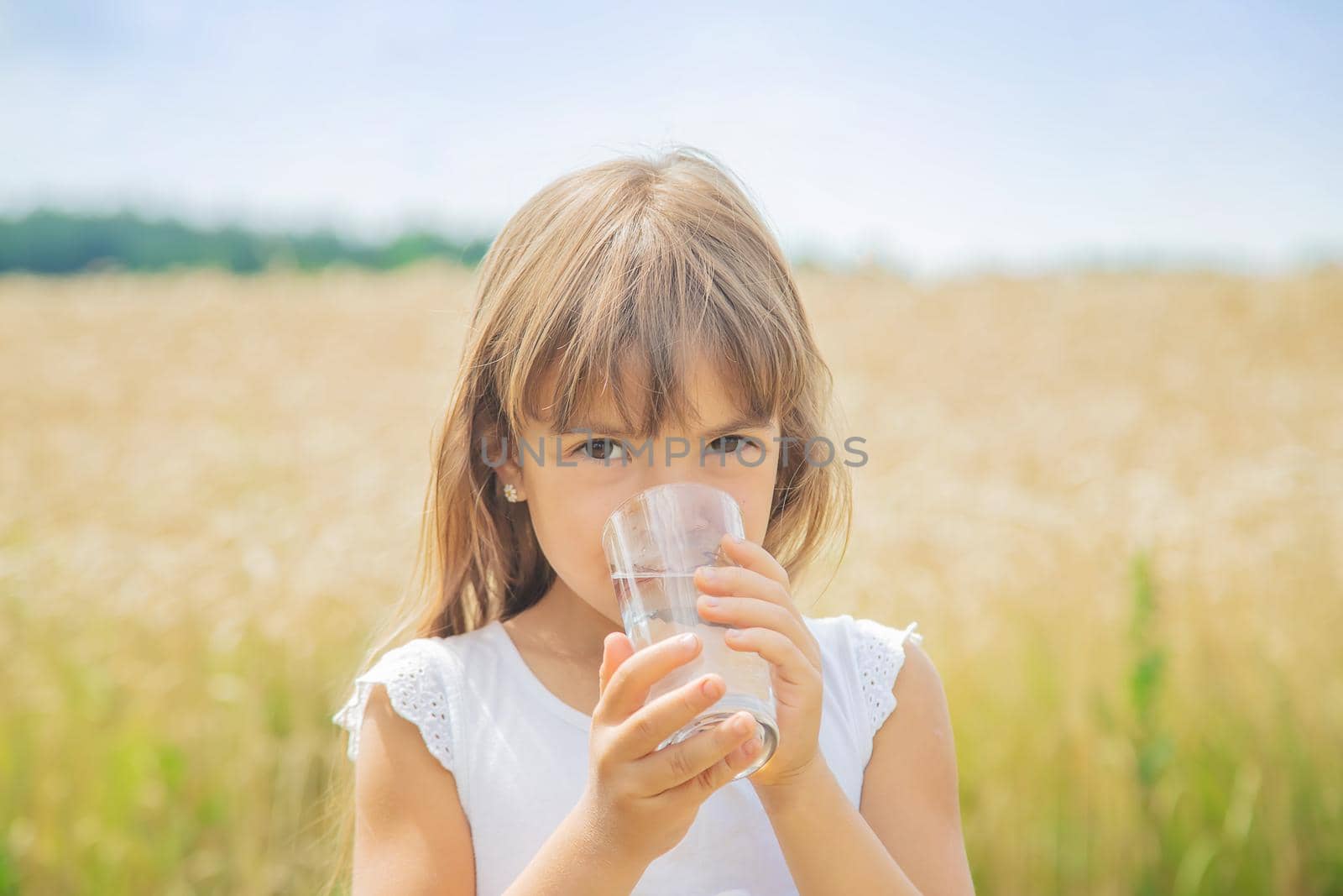 A child drinks water on the background of the field. Selective focus.