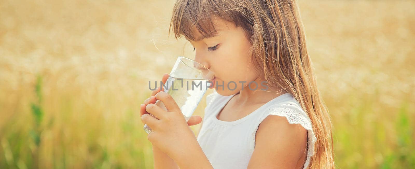 A child drinks water on the background of the field. Selective focus. by yanadjana