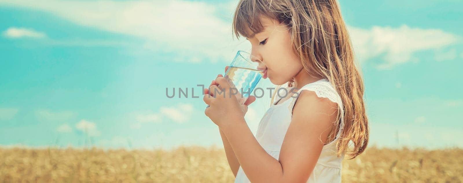 A child drinks water on the background of the field. Selective focus. by yanadjana