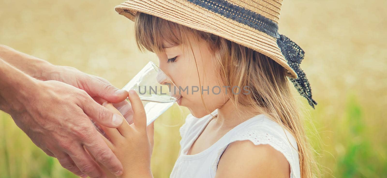 The father gives the child water in the background of the field. Selective focus.