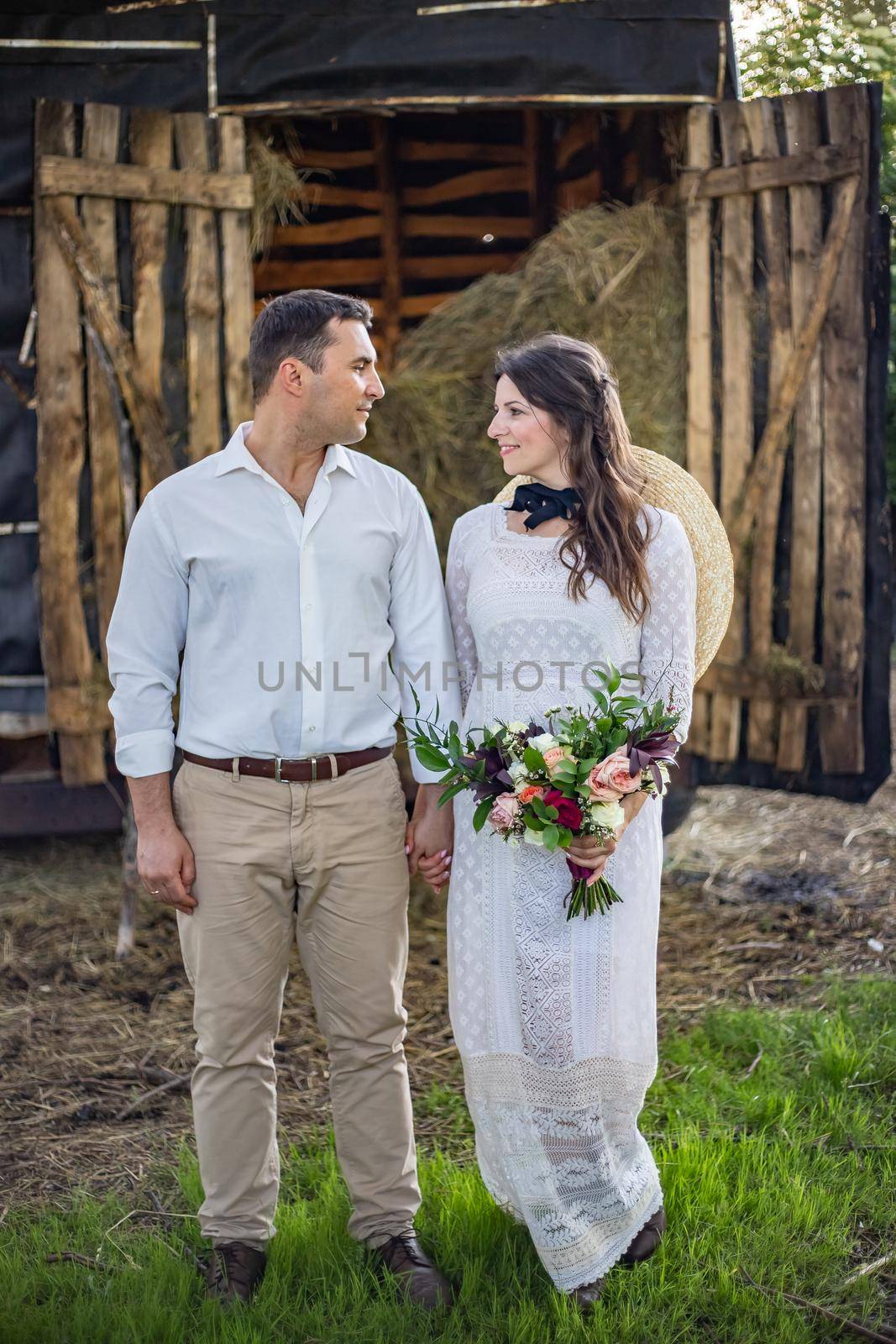 Beautiful wedding couple. The groom hugs the bride tightly and kisses. The bride holds a bouquet and laughs. Rustic wedding in the style of boho at the ranch