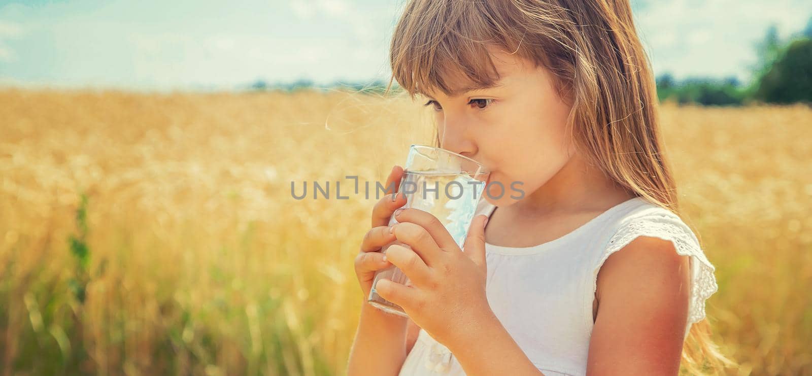 A child drinks water on the background of the field. Selective focus. by yanadjana