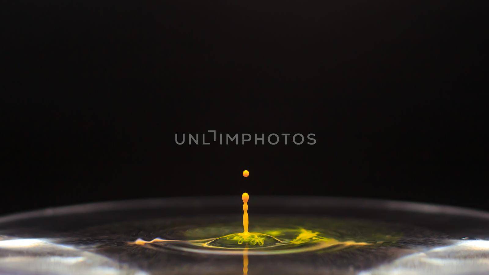 Yellow color water drop falling in water, freezing the moment