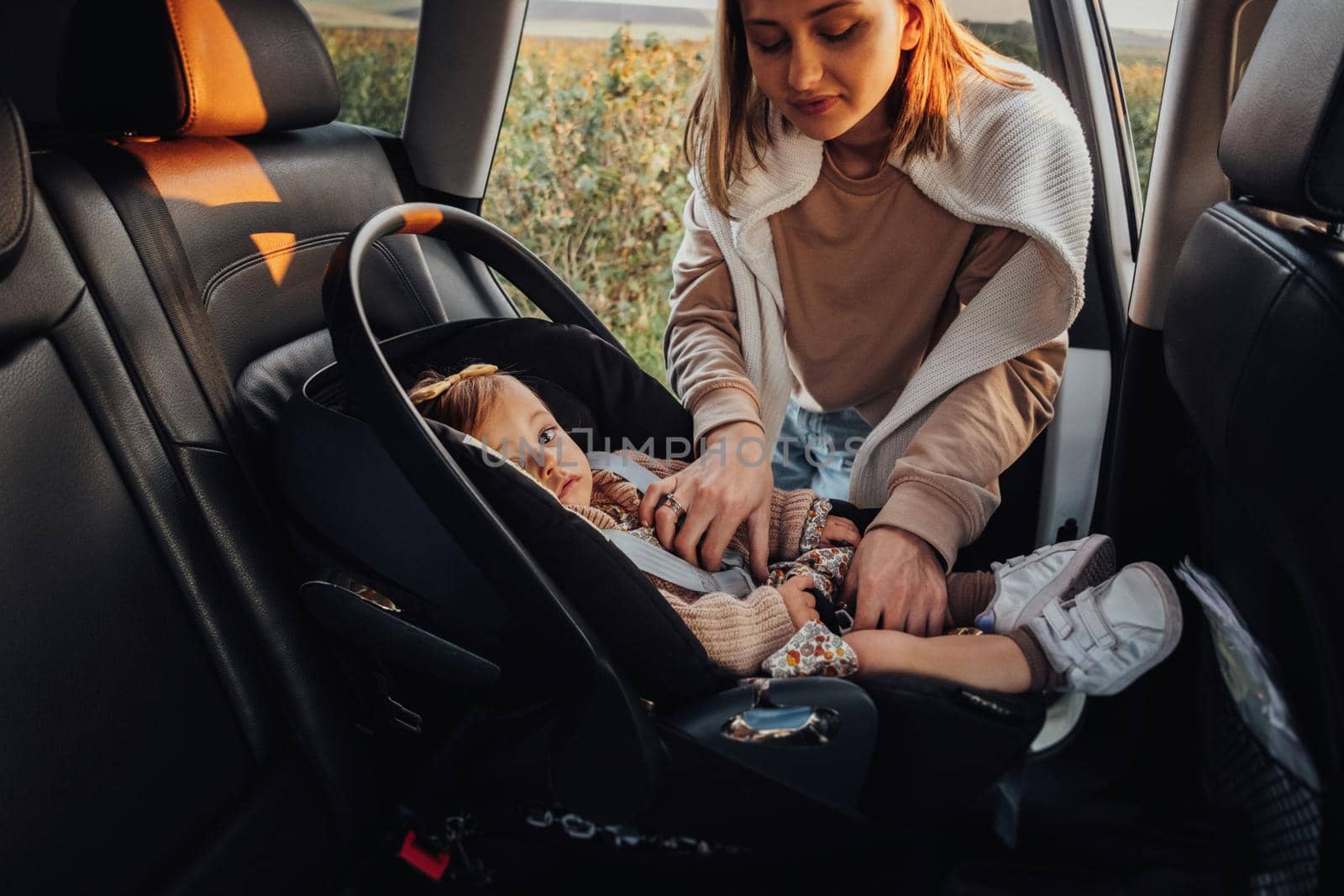 Young Mother Puts Her Baby Daughter in a Child Car Seat in Car