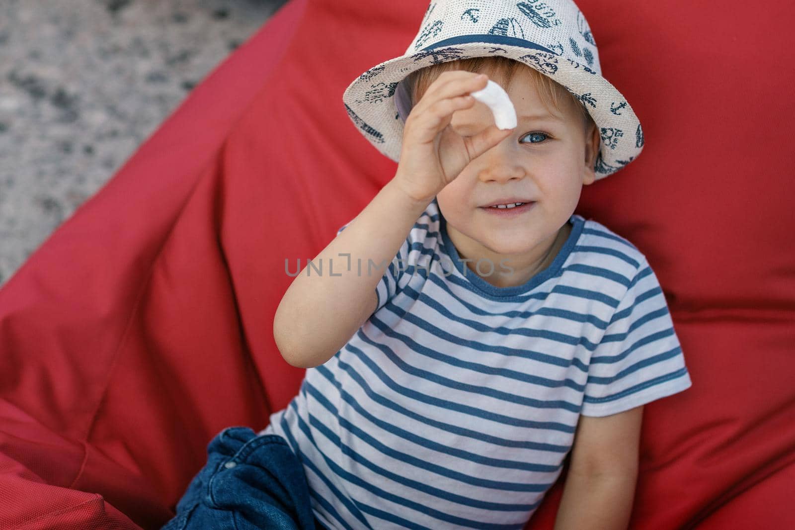 A little boy in a striped shirt and hat on a red background.