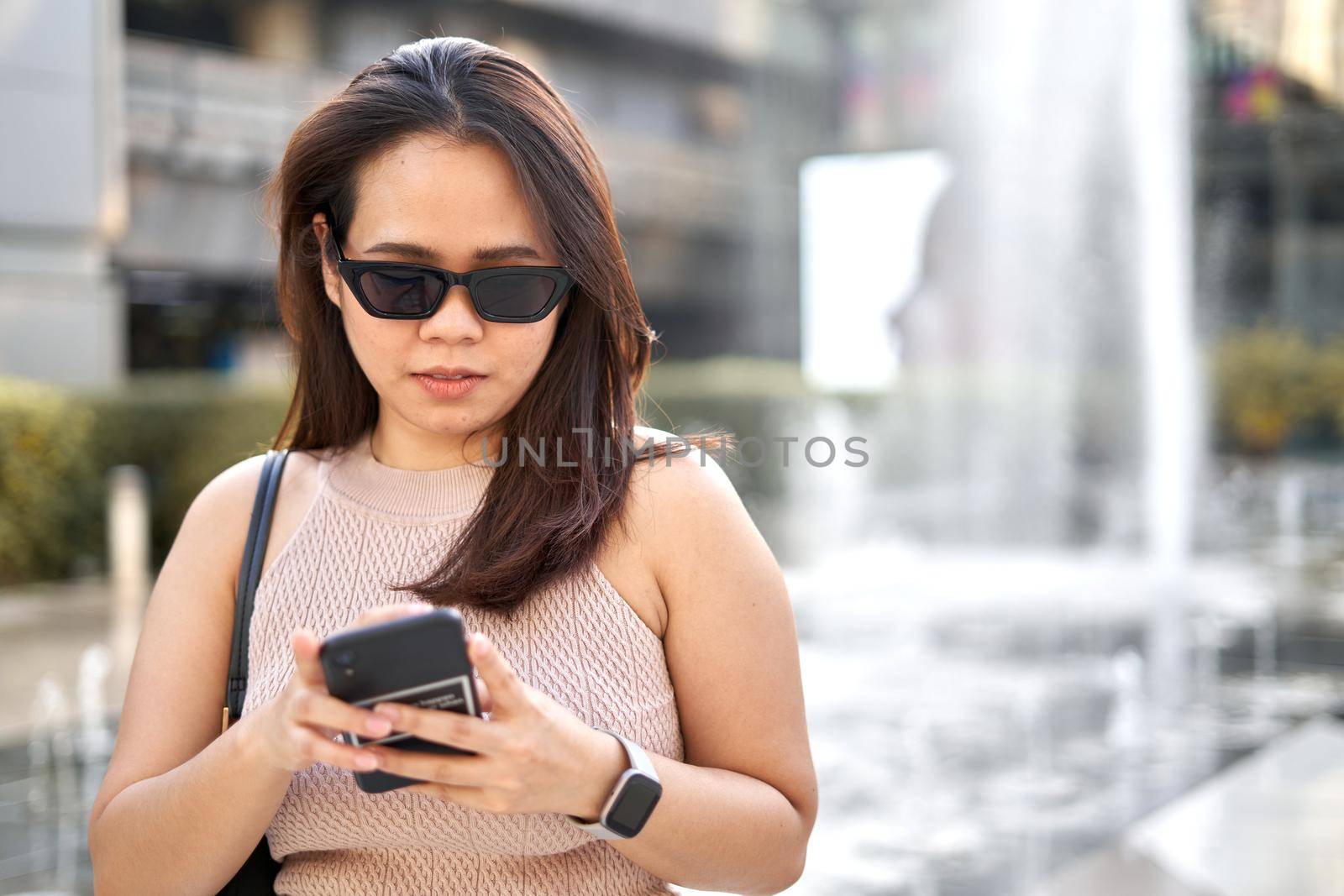 Portrait of an asian woman using the mobile while wearing sunglasses outside a mall