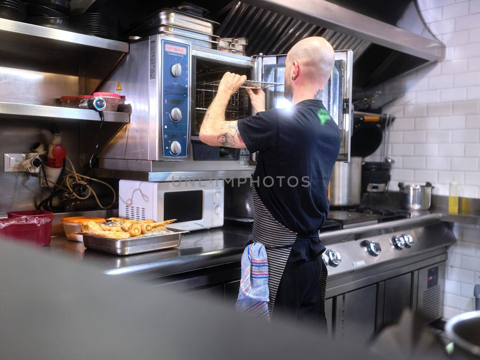 Back of a cook in an apron working in a restaurant kitchen preparing the oven