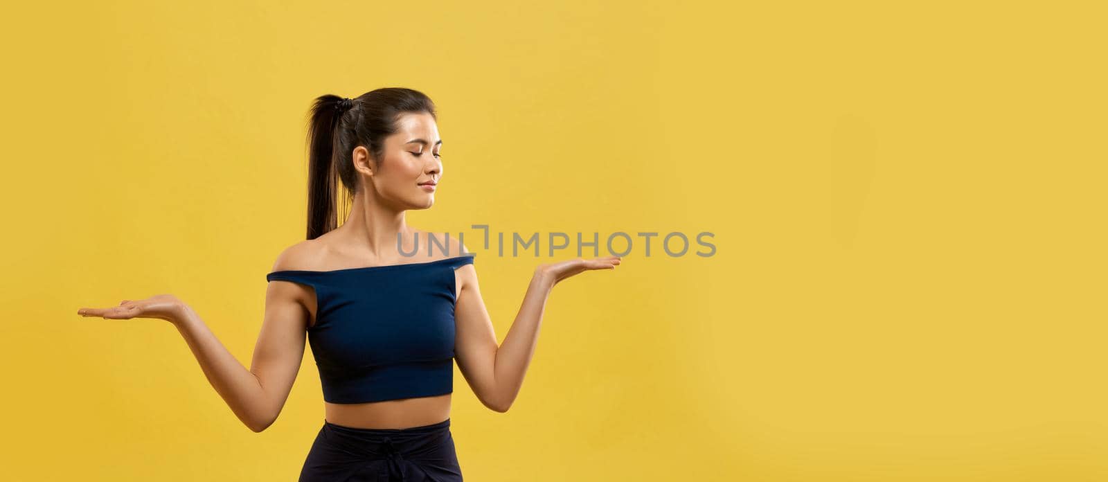 Attractive woman standing on knees, keeping hands palms up in studio. by SerhiiBobyk