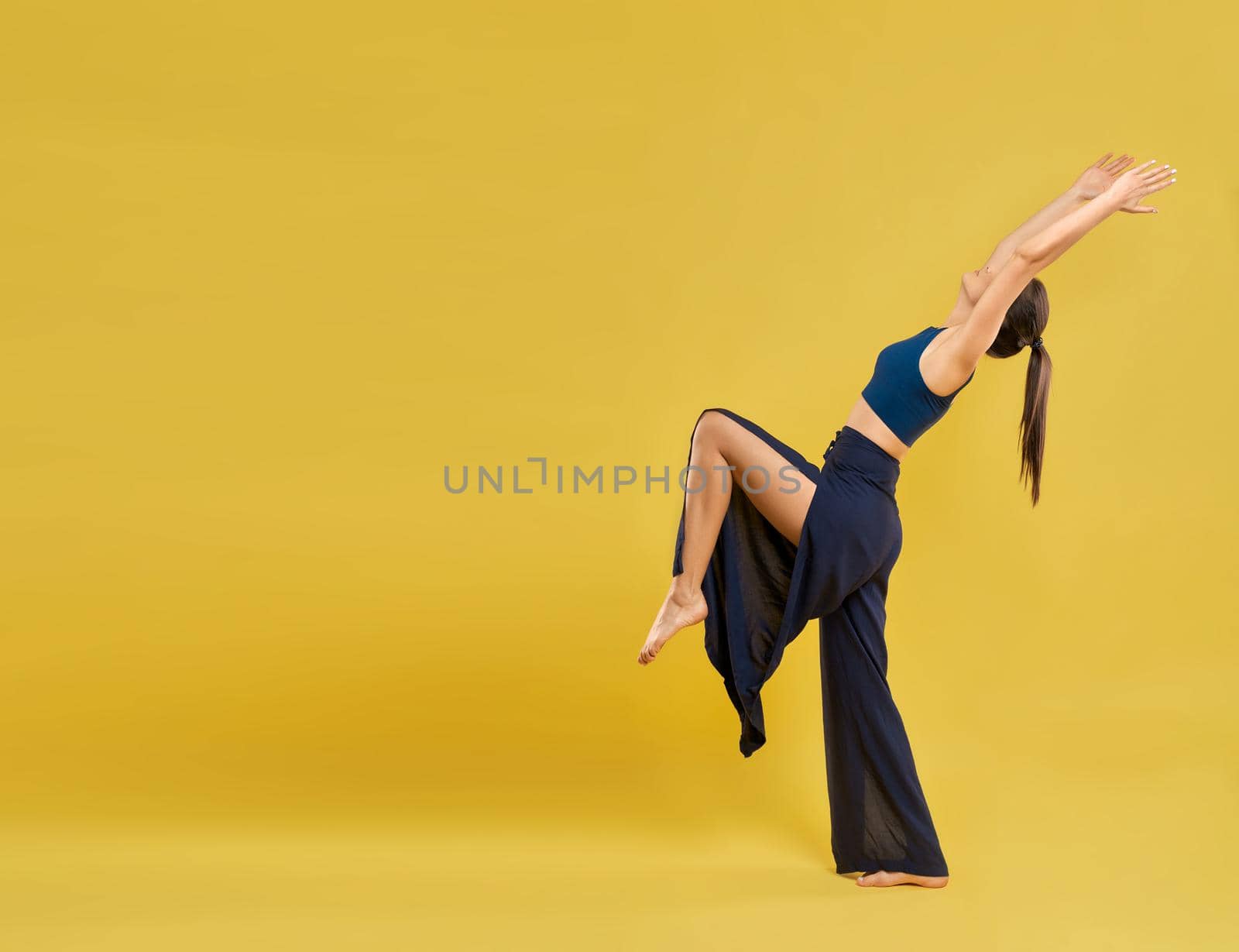 Modern female dancer wearing wide slits pants, performing dance poses and movements outdoors. Yogi girl practicing yoga, with copy space, isolated on orange studio background. Concept of lifestyle.