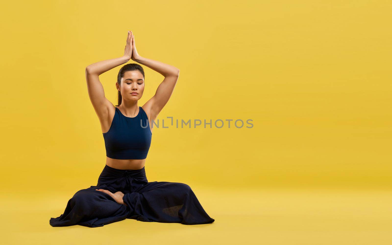 Attractive girl raising hands up with namaste gesture, praying in studio. Front view of young calm woman meditating with closed eyes, isolated on tangerine studio background. Concept of meditation.