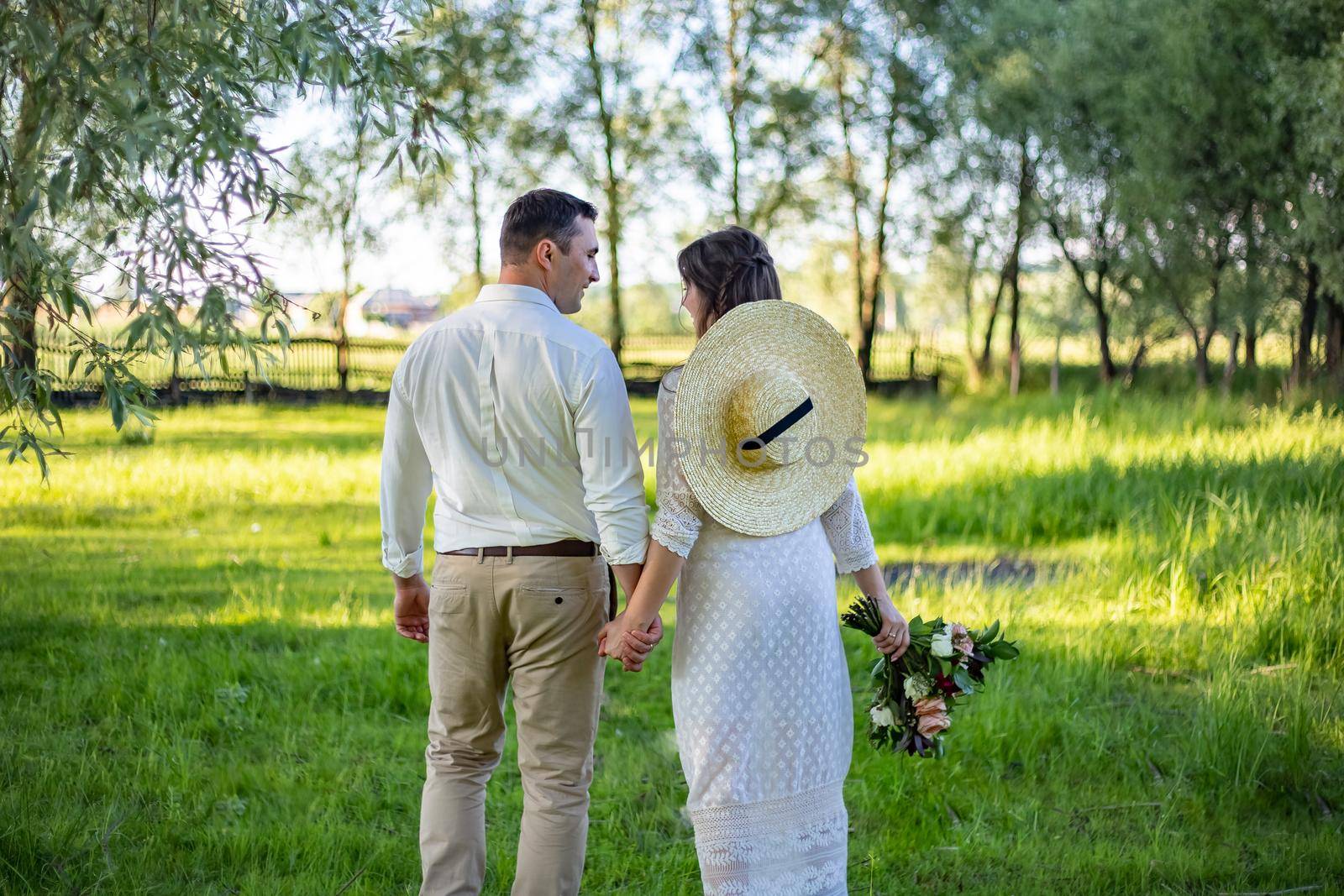 Just married loving hipster couple in wedding dress and suit on a green field in the woods. happy bride and groom walking running and dancing on a summer meadow. Romantic married to a young family.