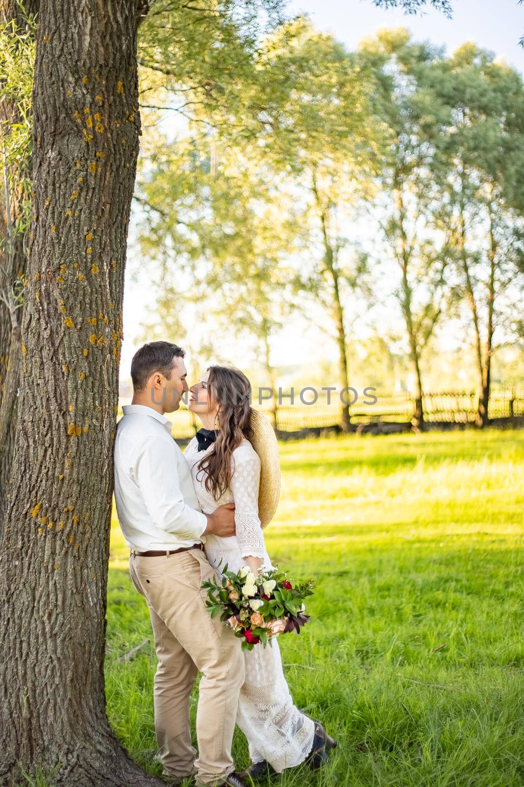 Happy young couple in green wheat field on their wedding day. Smiling newlyweds walking in the nature, holding hands. Family life, wedding concept