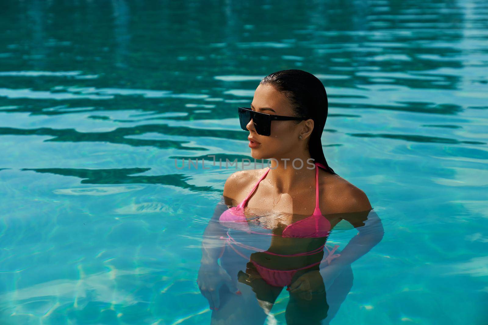 Pretty young female with long wet hair swimming in pool. by SerhiiBobyk