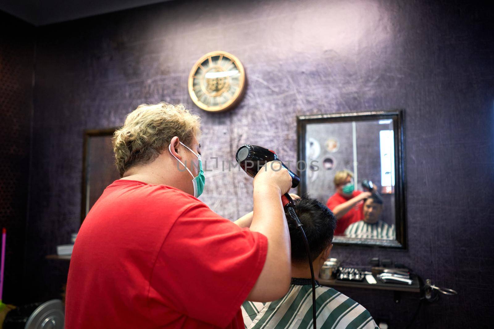 Back of a fat barber drying the hair of a client using an electric hairdryer