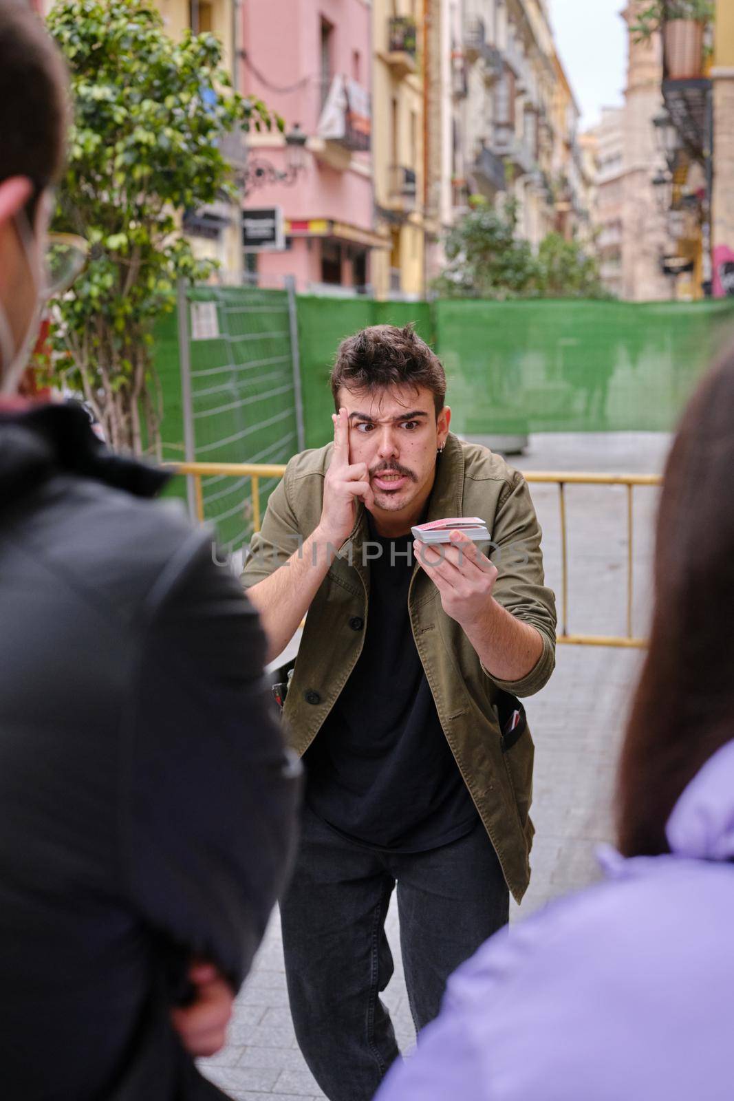 Vertical photo of a street magician making a gesture of concentration while doing a card magic trick