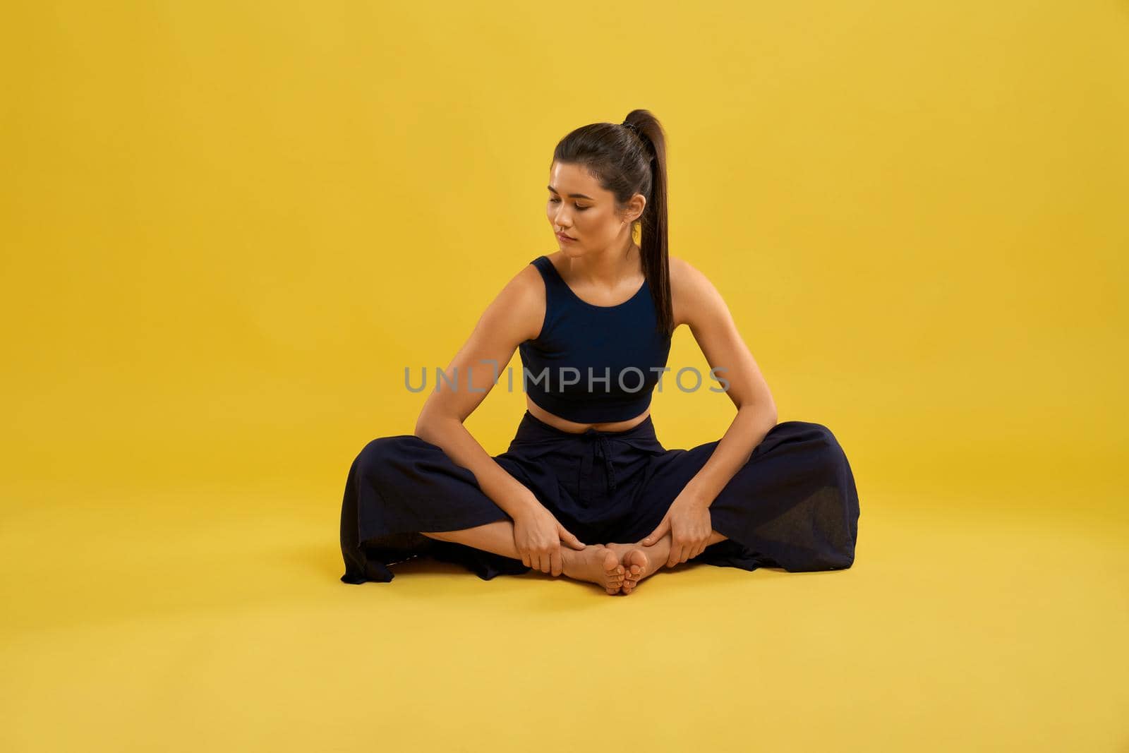 Pretty girl sitting in butterfly II yoga pose, with closed eyes and turned head while exercising. Front view of barefoot woman practicing yoga, isolated on orange studio background. Concept of yoga.