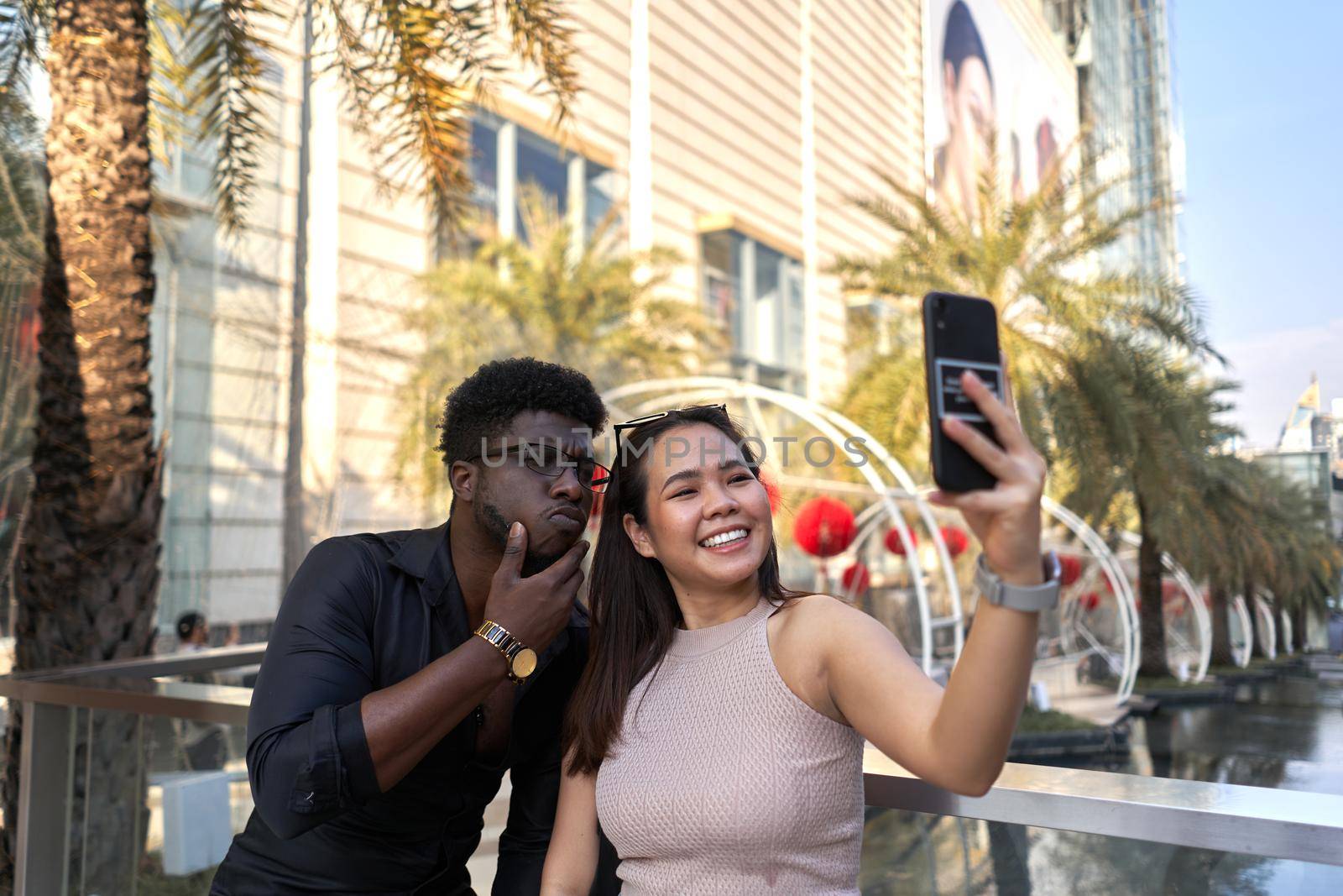 Two smiling friends of different ethnicities taking a selfie in the street in Bangkok, Thailand