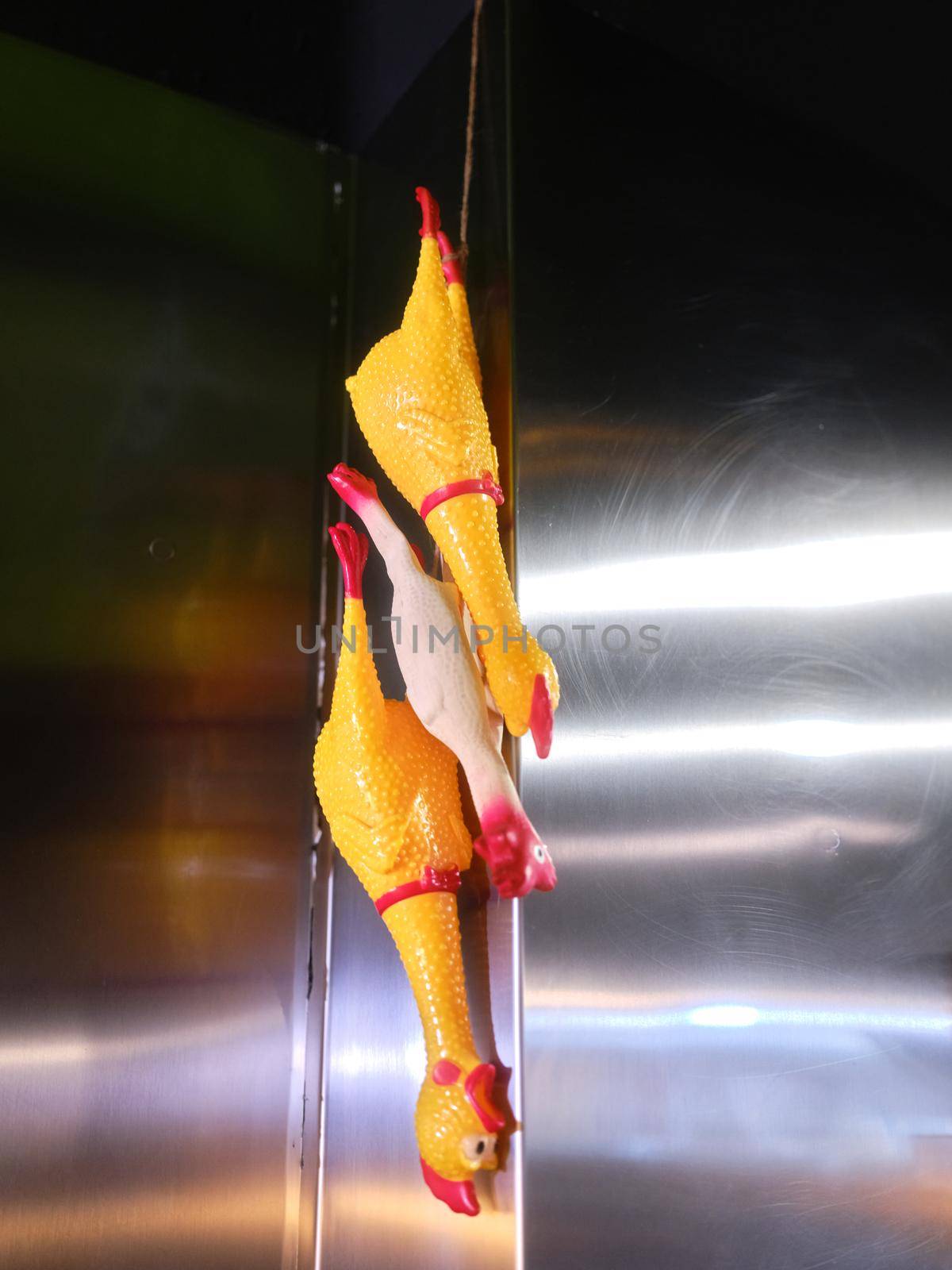 Three plastic chicken figures hanging from metal furniture wall in a restaurant kitchen