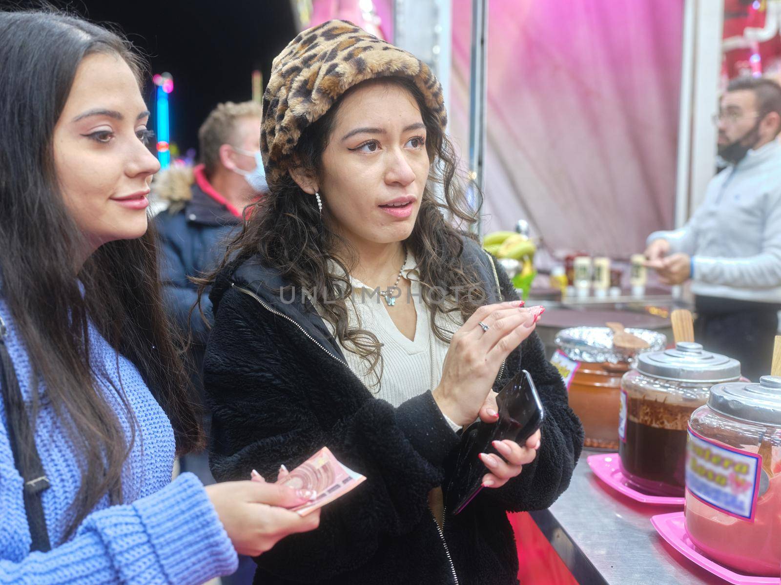 Profile of two latina women buying candy at a stop at an outdoors night fair