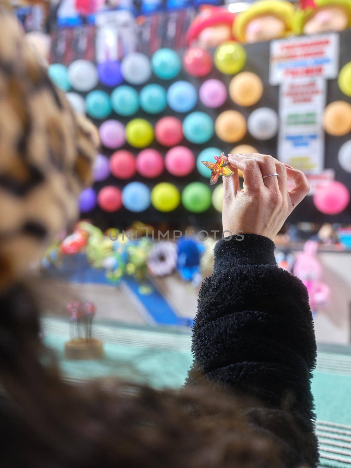 Vertical photo with focus on a woman's hand throwing a dart at a night-time fair