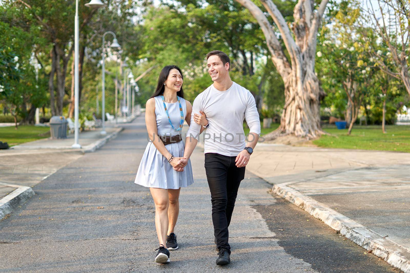 Newly married multicultural couple walking together on a path in a city park during sunset in summer