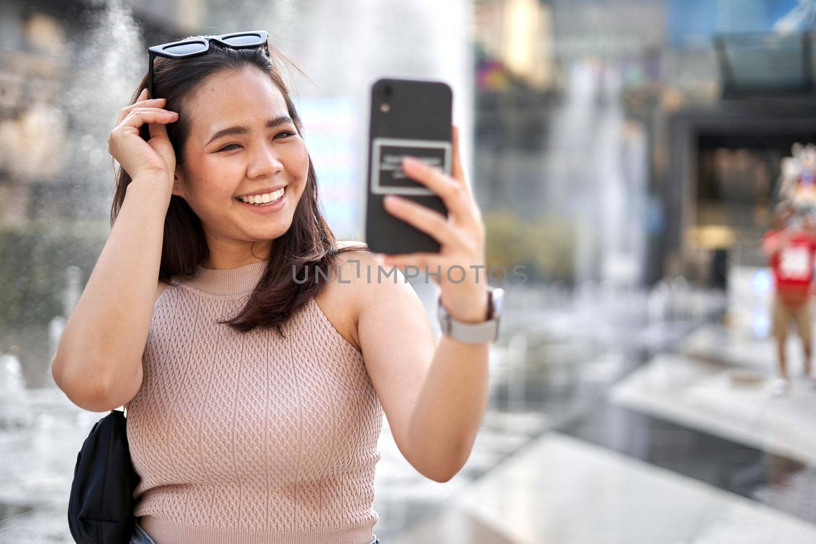 Asian woman in summer clothes smiling while taking selfie outside a shopping mall in Bangkok