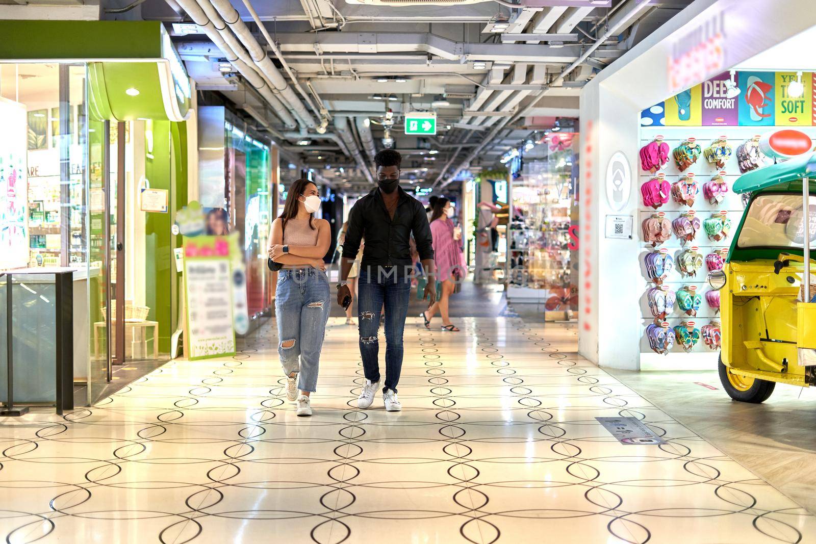 Multiethnic friends wearing mask and walking relaxed through a shopping mall passage between shops